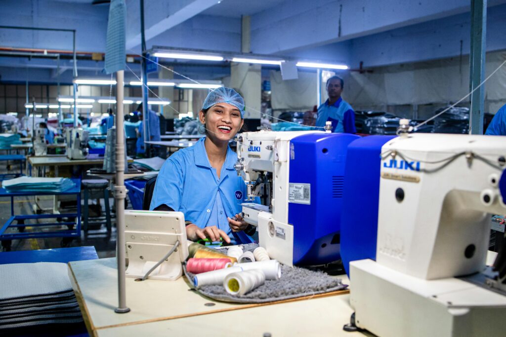 A cheerful textile worker operates a sewing machine in an industrial textile factory setting.